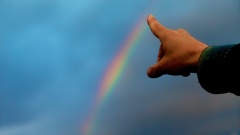 Zeigefinger zeigt auf Regenbogen am Himmel