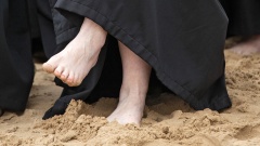 Pfarrerin im Talar mit nackten Füßen am Strand