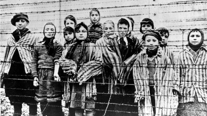 Kinder stehen nach der Befreiung des Konzentrations- und Vernichtsungslagers Auschwitz-Birkenau hinter Stacheldraht.