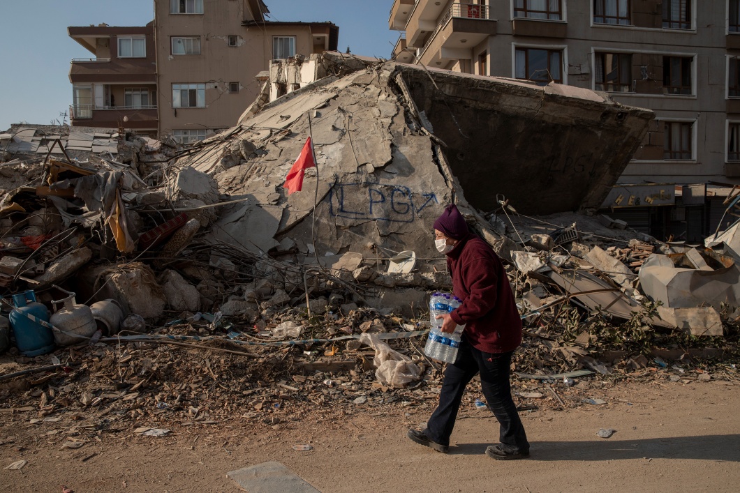 Eine Frau trägt Trinkwasserflaschen durch das verwüstete Hatay in der Türkei. Viele tausend Menschen haben durch das Beben ihre Wohnungen und Häuser verloren.
