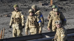 Ukrainische Soldaten gehen am 26.02.2022 in der Nähe von Trümmern eines brennenden Militärlastwagens auf einer Straße in Kiew. 