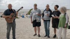 Pastor Fritz Baltruweit singt mit Menschen am Strand.