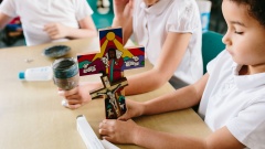 Kinder am Schultisch basteln ein Kreuz.
