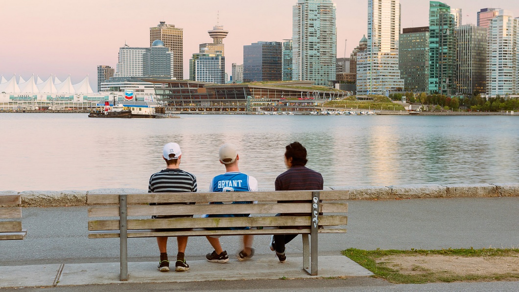 Menschen sitzen auf einer Bank vor der Skyline von Vancouver