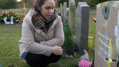 junge Frau kniet vor Kindergrab auf einem Friedhof