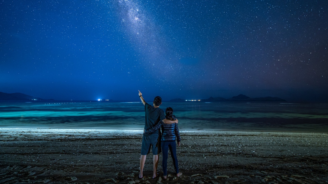 Paar steht am Meer mit Blick auf den Sternenhimmel