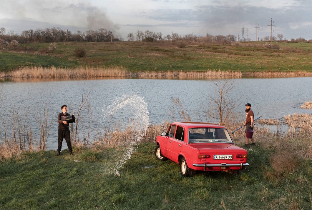 Weder das Donnern der Artillerie noch der Rauch der Bombenangriffe hält Sergei und Dima davon ab, den alten roten Lada zu waschen. Tschassiw Jar, Ukraine, 10. April 2023.
