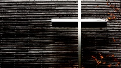 Foto zeigt silbernes Kreuz an der dunkel-hölzernen Außenseite einer Kirche