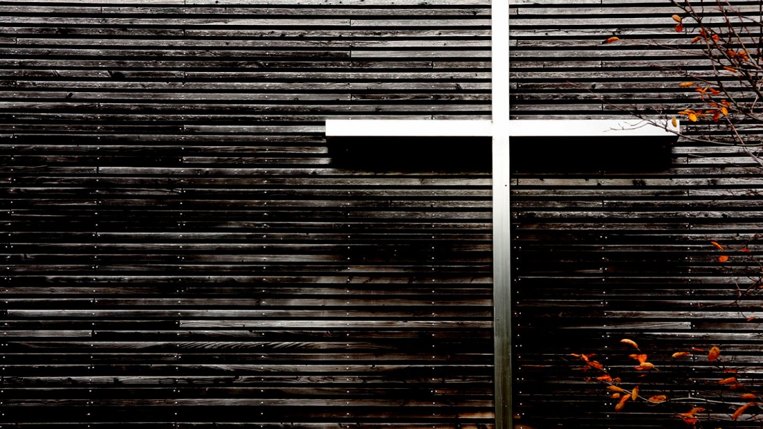 Foto zeigt silbernes Kreuz an der dunkel-hölzernen Außenseite einer Kirche