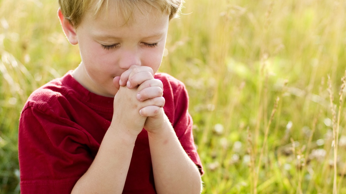 Ein Junge hat die Hände zum Gebet gefaltet.