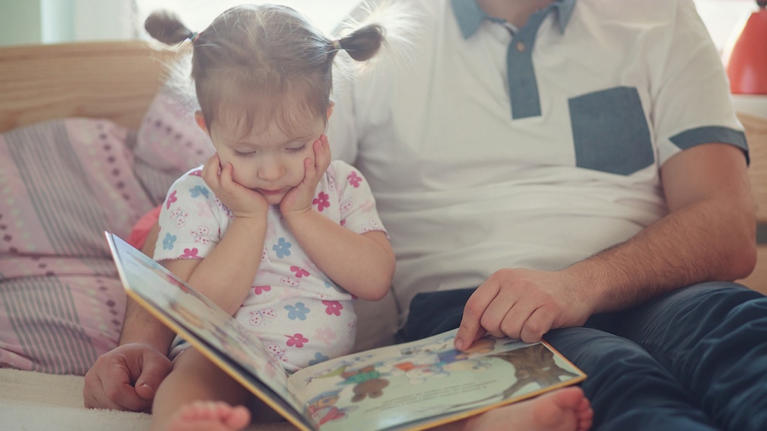 Vater liest seiner kleinen Tochter aus einem Bilderbuch vor.