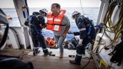 Ein Mann in Rettungsweste steigt auf die "Sea-Watch 4" und wird dort von den Crew-Mitgliedern in Empfang genommen.