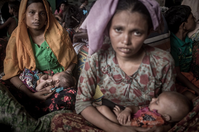 Zwei Rohingya Flüchtinge. Beide halten Babies in den Händen und sehen erschöpft in die Kamera