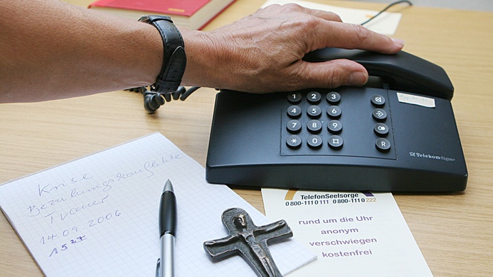 Telefon, Stift, Papier und ein Kreuz auf einem Tisch