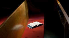 Ein Gesangbuch liegt auf einer leeren Kirchenbank.