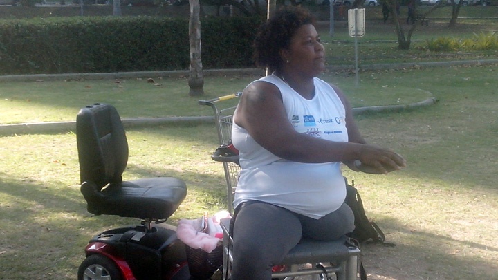 Rosinha dos Santos sitzt auf einem Gestell in einem Park und trainiert, im Hintergrund steht ihr Rollstuhl.