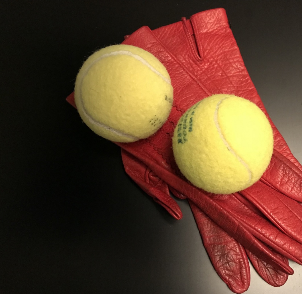 Zwei gelbe Tennisbälle auf roten Handschuhen und schwarzem Grund 