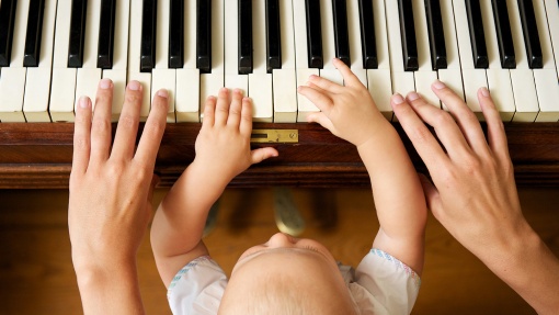 Babyhände und große Hände auf den Tasten eines Klaviers.